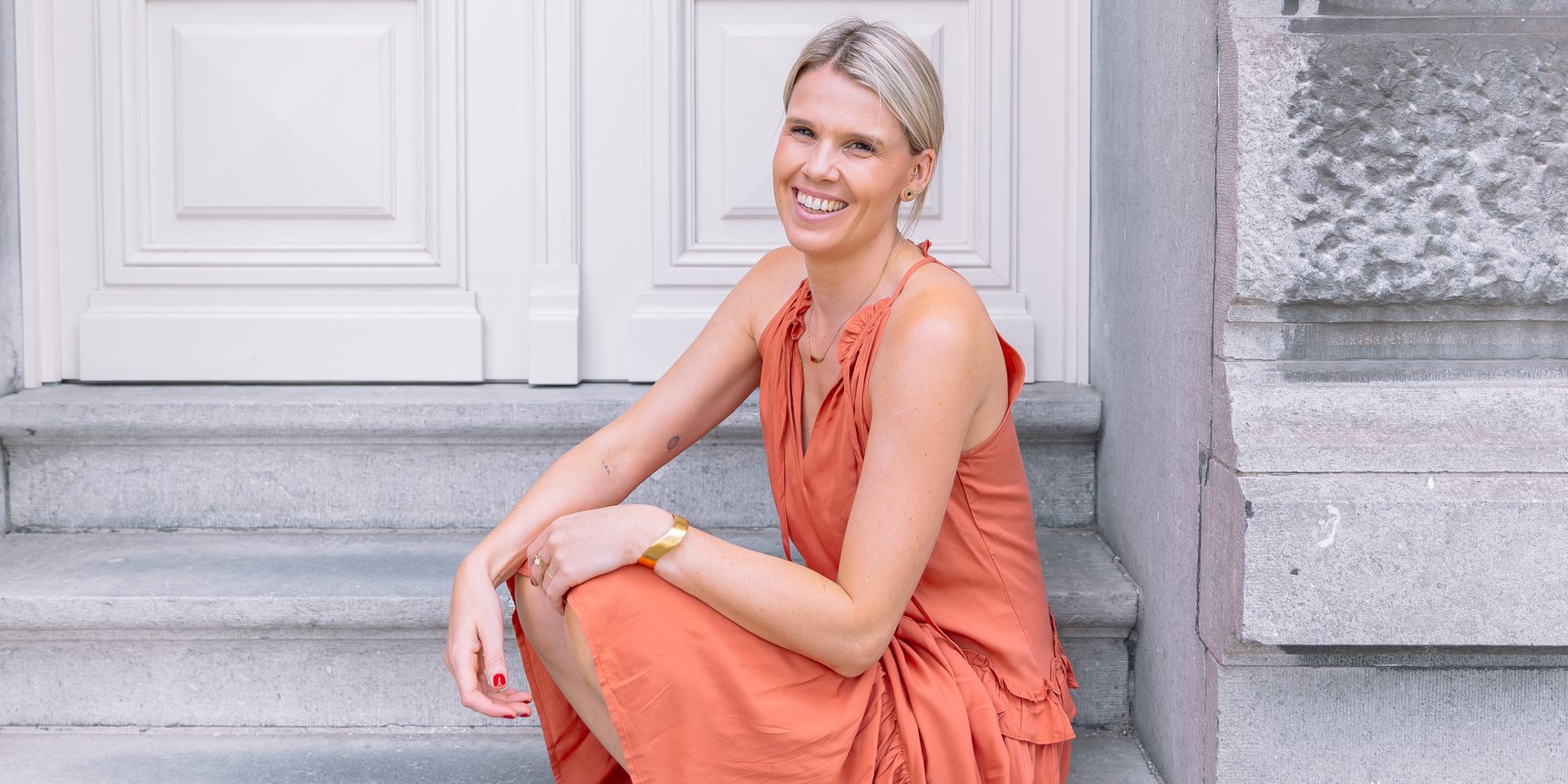 Sarah van club sol, in haar terracotta jurk op de trappen in Antwerpen